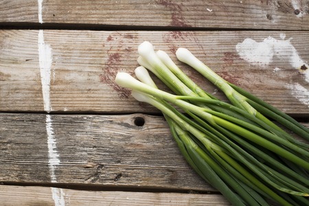 A bunch of fresh young green spring onion on a simple wooden background in rustic style. The concept of cooking with seasonal ingredients and organic pitanif. Horizontal. Free space for textの写真素材
