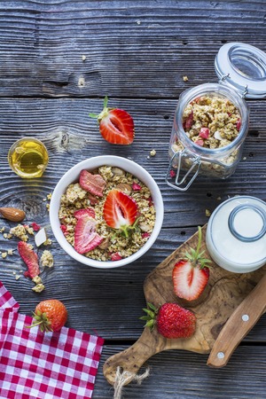Ready-made granola with dried strawberries and almonds. Healthy breakfast with cereal muesli, dried and fresh strawberries, almonds, milk, honey, a simple wooden background in rustic style. selective focusの写真素材