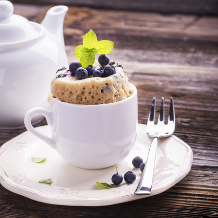 Healthy breakfast. Fresh homemade mug cake with forest blueberries in a white ceramic bowl with a sprig of ripe berries on the gray wooden background. selective focusの写真素材