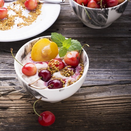 Healthy breakfast snack. Marble Portion bowl full of cherry smoothie with natural yogurt, ripe berries, fruits, bee pollen, berry syrup on a wooden background. selective focusの写真素材