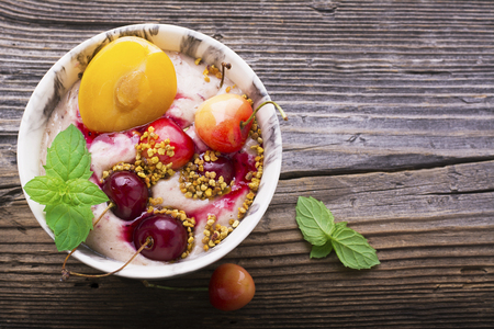 Healthy breakfast snack. Marble Portion bowl full of cherry smoothie with natural yogurt, ripe berries, fruits, bee pollen, berry syrup on a wooden background. selective focusの写真素材