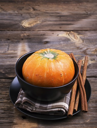 Autumn themed tableware. Black pottery, long cinnamon sticks, small ripe pumpkin on a simple wooden background. selective focusの写真素材