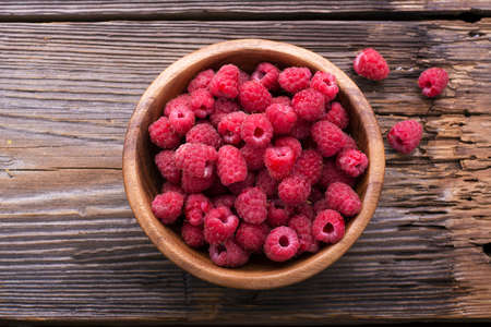 A wooden bowl full of ripe juicy fragrant garden raspberries on a simple rustic wooden background....