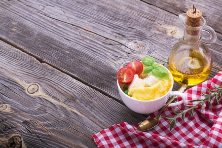 Quick simple breakfast snack for a few minutes in the microwave. Fragrant bright omelette with slices of white bread, herbs, juicy tomatoes with oil in white cup portions for healthy homemade food. With ripe peppers and basil. selective focusの写真素材