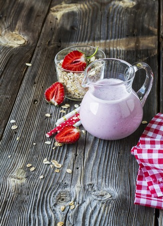Glass jug with fresh home village milkshake with fresh strawberries on a gray wooden background. Served with berries and colored tubes. selective focusの写真素材