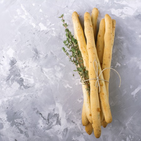 Fresh homemade crispy bread sticks with thyme and sea salt on a gray concrete background with fresh herbs. selective focusの写真素材