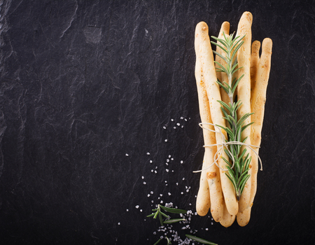 Fresh homemade crispy bread sticks with thyme and sea salt on a black background with fresh herbs....