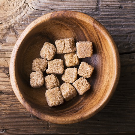 Cubes natural brown cane sugar in a wooden bowl on a wooden background. The concept of natural organic food. Selective focus. View from aboveの写真素材