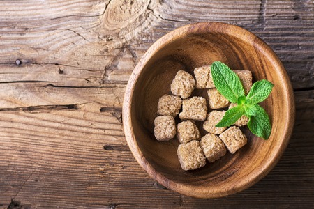 Cubes natural brown cane sugar in a wooden bowl on a wooden background. The concept of natural organic food. Selective focus. View from aboveの写真素材