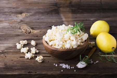 Salty crunchy fresh homemade popcorn flavored with lemon peel and rosemary scent in a wooden bowl on a simple wooden background. The concept of natural homemade organic seasonal food. selective focusの写真素材