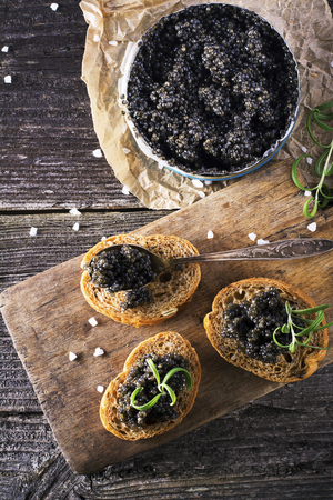 Black Astrakhan Russian salted sturgeon caviar in a can on a dark background with a wooden spoon and slices of bread. Snacks and luxury holidays. selective focusの写真素材