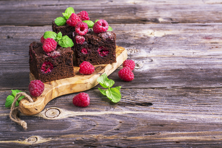 Simple fresh homemade brownies flavored with berries juicy fresh ripe raspberry on wooden background decorated with mint. Selective focus in the horizontal designの写真素材