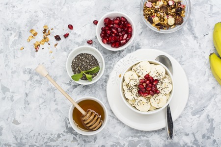 Healthy breakfast oatmeal with pomegranate, bananas, seeds and nuts, overhead scene on white marbleの写真素材