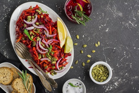 Vegetable salad on the basis of beet, carrot, sweet onion salad, pumpkin seeds in an oval ceramic dish on a dark background. Top viewの写真素材