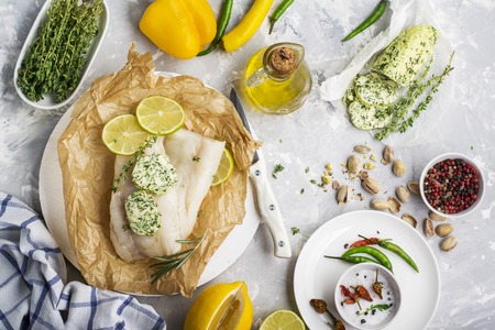 Cod fillet on parchment with lemon and green butter with herbs and savory pistachio crust before baking. Top view. On a light background.の写真素材