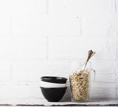 Simple kitchen still life with ceramic cups of contrast, a tall glass  oat flakes in one piece for the preparation  healthy wholesome breakfast comfort food on  background   white brick wall.の写真素材