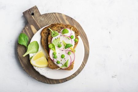 Healthy snack: slice grain bread with ricotta, green peas, radishes, lemon zest and juice. Top viewの写真素材