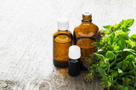 Essential oregano oil for aromatherapy in a dark glass containers on wooden background with fresh oregano. Selective focus.の写真素材