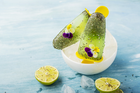 Magnificent homemade yellow-green fruit vegetarian lactose-free ice cream with chia seeds, fruit juice, limes with edible flowers and garden violas on a light background.の写真素材