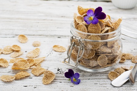The concept of a healthy breakfast of whole wheat cereals, berries and edible flowers on a garden violet on a light wooden background in a glass jar. Selective focusの写真素材