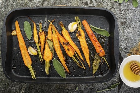 Young juicy carrots baked with honey, sage, garlic, olive oil, salt for a homely comfortable dinner on the background. Top View.の写真素材