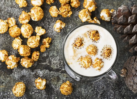 A glass of mouth-watering sweet milk coffee with a creamy foam topped with caramel crispy popcorn on...