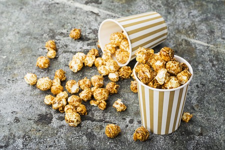 Appetizing homemade caramel popcorn in striped classic paper cups on a gray background. Selective focusの写真素材