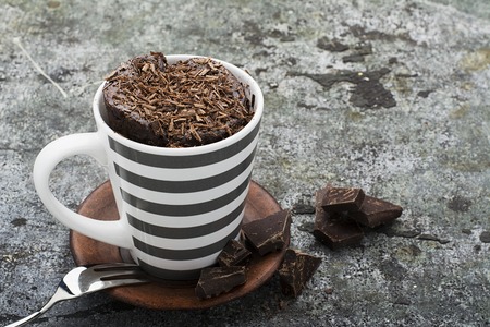 Homemade chocolate aromatic mug cupcake in a stylish gray striped mug on a gray stone background with bits of bitter chocolate. Selective focusの写真素材