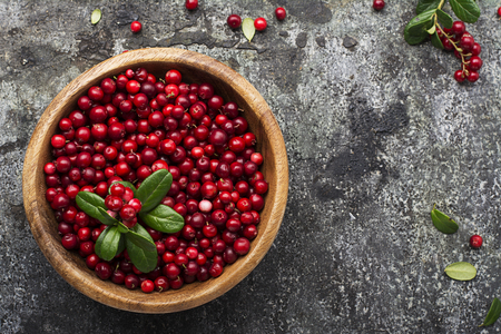 Ripe northern lingonberry in a wooden bowl on a background with twigs and leaves. Top Viewの写真素材