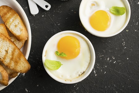 Breakfast for two. Eggs baked in the oven in ceramic portioned forms with toasted bread and slices of fresh cucumber. Top View.の写真素材
