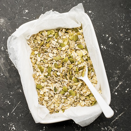 Ingredients for the preparation of baked crispy appetizing toping for thick autumn winter vegetable soups puree from pumpkin seeds, sunflower seeds, oat flakes in ceramic form on a dark background. Top View.の写真素材