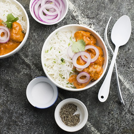 Homemade dinner butter chicken on cream with spices, cream served with basmati rice in ceramic bowls with cilantro and sweet red onion. Top Viewの写真素材
