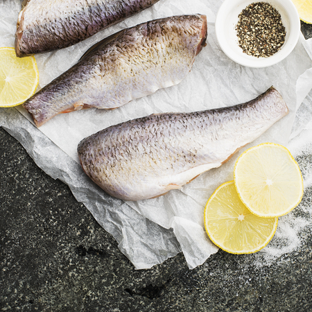 Fresh gutted cut river fish before cooking with salt, pepper, lemon slices on a gray grunge background. Top View.の写真素材