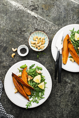 Baked slices of sweet potatoes for a vegetarian healthy snack lunch with salad, yoghurt sauce, black sesame served portioned in a plate. Top View.の写真素材
