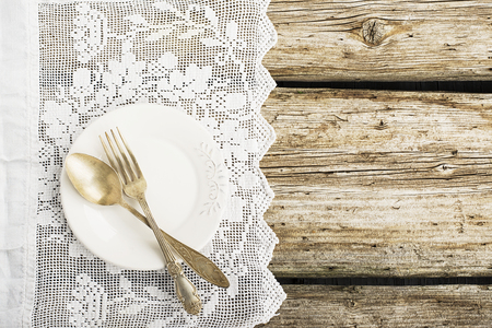 White ceramic plates on a simple wooden background with a white vintage lacy tablecloth with silverware table instruments with a pink paper heart. Top view. Copy space,の写真素材