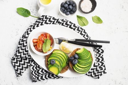 Sandwiches for a healthy breakfast with avocado and blueberries. Sliced cherry tomatoes and spinach for serving. Top view. Copy space.の写真素材