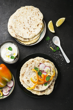 Traditional homemade flat breads for a snack with fresh seasonal vegetables, herbs and yoghurt sauce...