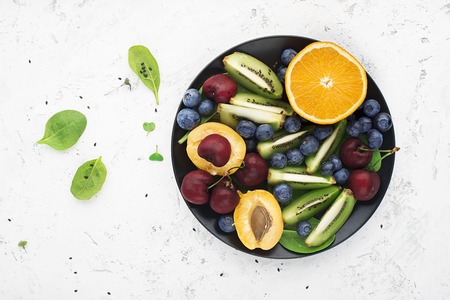 Fruit summer bowl. Orange, kiwi, cherry, spinach blueberry apricot plate Top Viewの写真素材