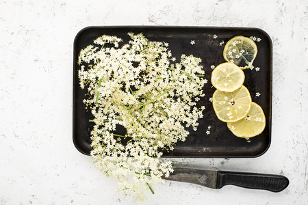Ingredients for a healthy homemade drink: elderberry flowers, lemon slices on a vintage black tray for making a recipe. Top viewの写真素材