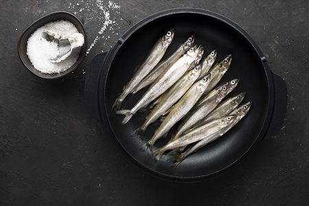 Small sea fish smelt or sardine before cooking in a cast-iron form for baking with lemon, butter and salt. Top view. On a dark background.の写真素材
