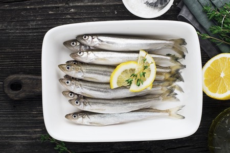Fresh sea cold-water small fish such as smelt, sardine, anchovies on a simple background with lemon...