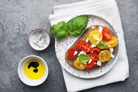 Healthy food. Cherry tomatoes, cottage cheese, young cheese, basil sandwiches, wholegrain bread with olive oil, balsamic sauce. Top view, space. On a gray dark background..の写真素材