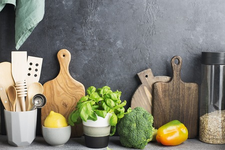 Kitchen table shelf with cutlery, spoons, spatulas, fresh basil, cutting boards, fresh vegetables,...