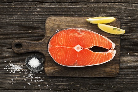 Raw salmon steaks before cooking on a wooden  with lemon, salt, rosemary. Top view.の写真素材