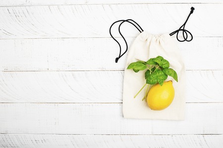 Lemon and basil on white cotton eco bag on white wooden background. The concept of no plastic zero waste house shopping. Copy space. Top viewの写真素材