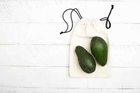 Avocado on white cotton eco bag on white wooden background. The concept of no plastic zero waste house shopping. Copy space. Top viewの写真素材