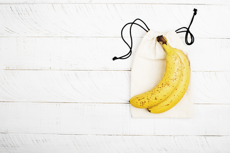 Bananas on a white cotton eco bag on a white wooden background. The concept of no plastic zero waste house shopping. Copy space. Top view.の写真素材