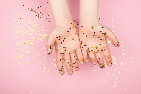 Gold glitter stars confetti on hands on a gentle pastelの写真素材