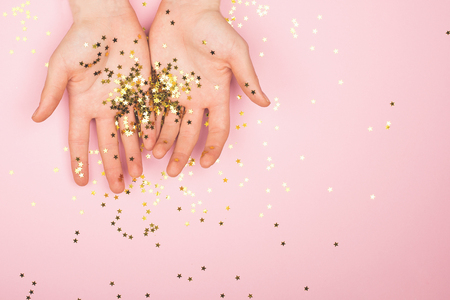 Gold glitter stars confetti on hands on a gentle pastelの写真素材