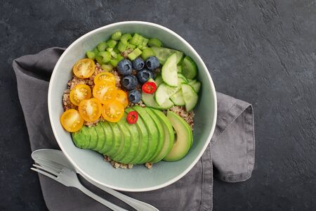 Healthy vegetable wholegrain bowl. Quinoa, avocado, cherry tomatoes, juicy celery, blueberries, hot peppers balanced lunch breakfast. Without meat. Top view. On a dark backgroundの写真素材